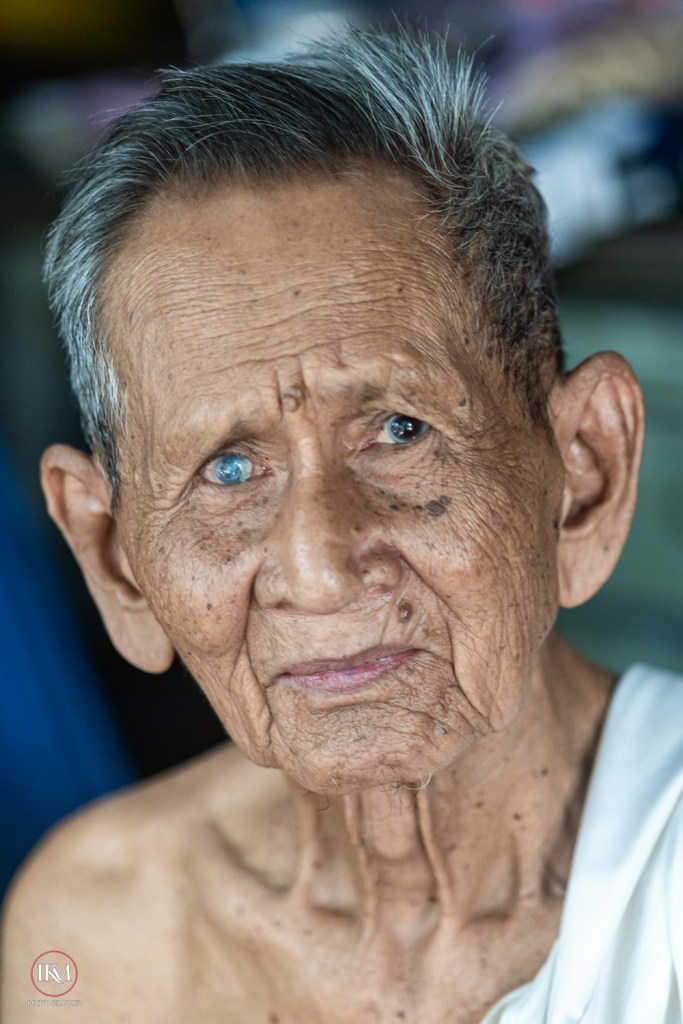 Close-up portrait of an elderly man with gray hair and deep wrinkles, wearing a traditional garment.
