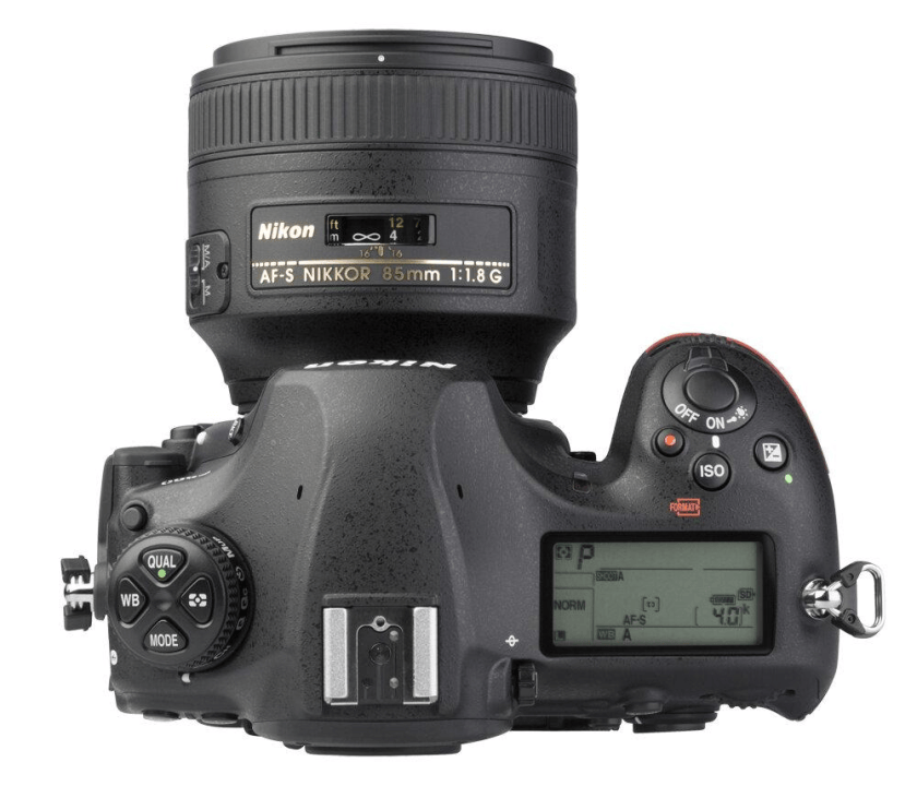 Top view of a Nikon camera with an AF-S NIKKOR 85mm f/1.8G lens attached, displaying various buttons and the digital screen showing settings.
