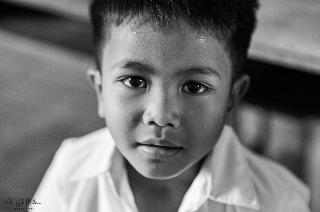 Close-up portrait of a young boy with a serious expression, wearing a white shirt, captured in black and white.