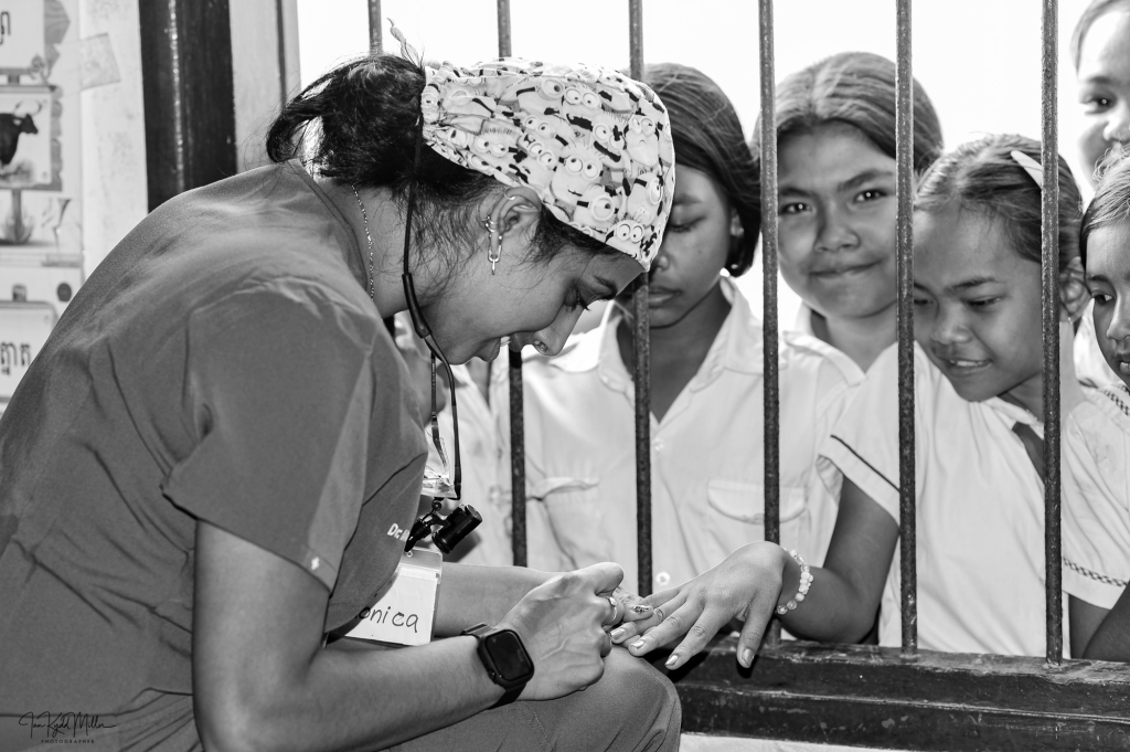 A healthcare worker in scrubs is examining the hand of a child through a barred window, while several other children watch attentively.