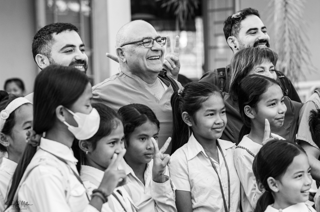 A group of smiling adults and children posing together for a photo, with some individuals making peace signs. The image is in black and white.
